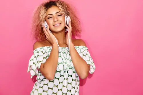 Fashion happy beautiful black woman with afro blond hair.Girl smiling and listening to music in headphones. Playful hipster model posing near pink wall 1203