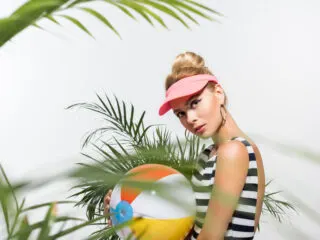 cute beachy woman surrounded by palm trees holds a beach ball and contemplates the meaning of angel number 3838