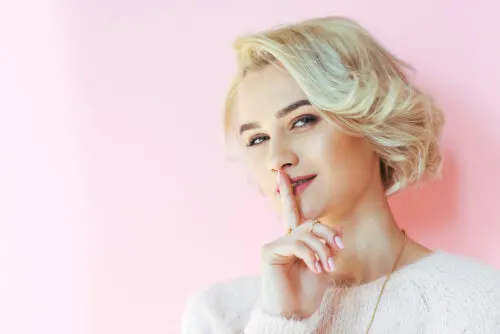 blonde woman making the "shhh" sign on a pink background thinking of 369.
