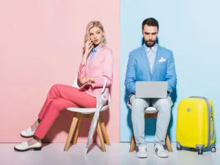 suspicious pink woman and blue man sitting side by side kind of not talking to eachother but on their laptop and phone with luggage and an umbrella